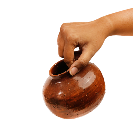 A hand holding a small, rounded brown ceramic pot with a glossy finish against a solid white background.